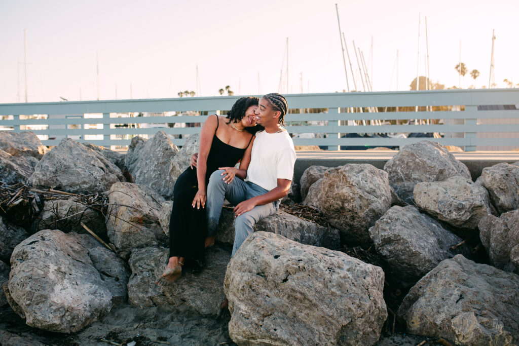 The lift: Groom-to-be lifting his fiancée in the surf at a Santa Barbara beach at sunset
Rocks, wide: Couple sitting together on the breakwater rocks at Santa Barbara Harbor at sunset
